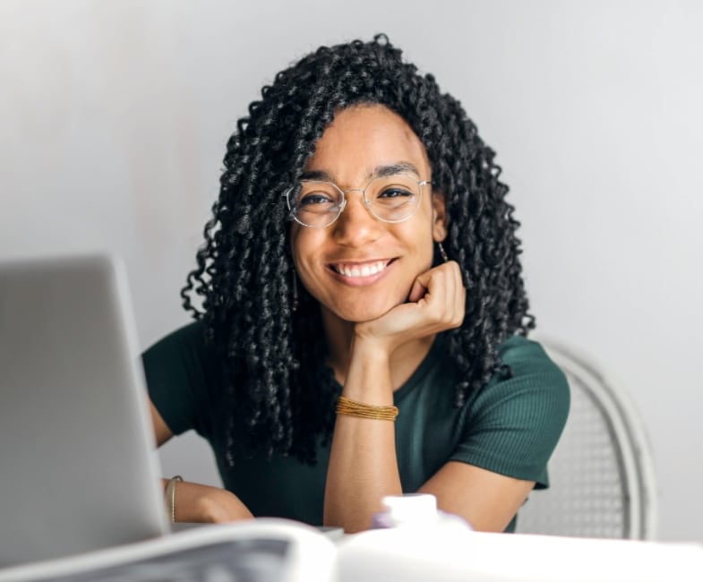 A person sitting at a desk with a computer and smiling at the camera